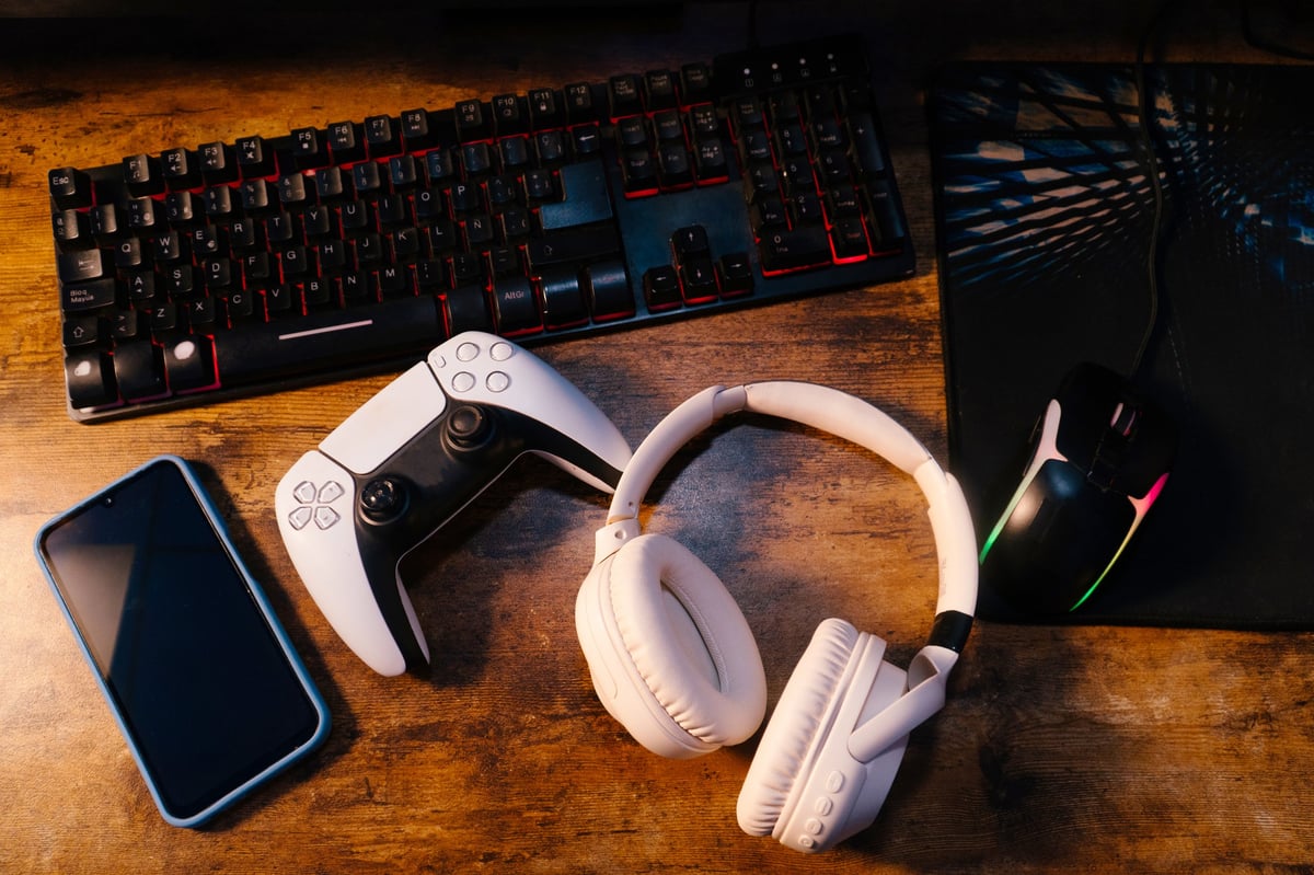 Gaming accessories including a console controller, keyboard, headphones and mouse on a wooden surface